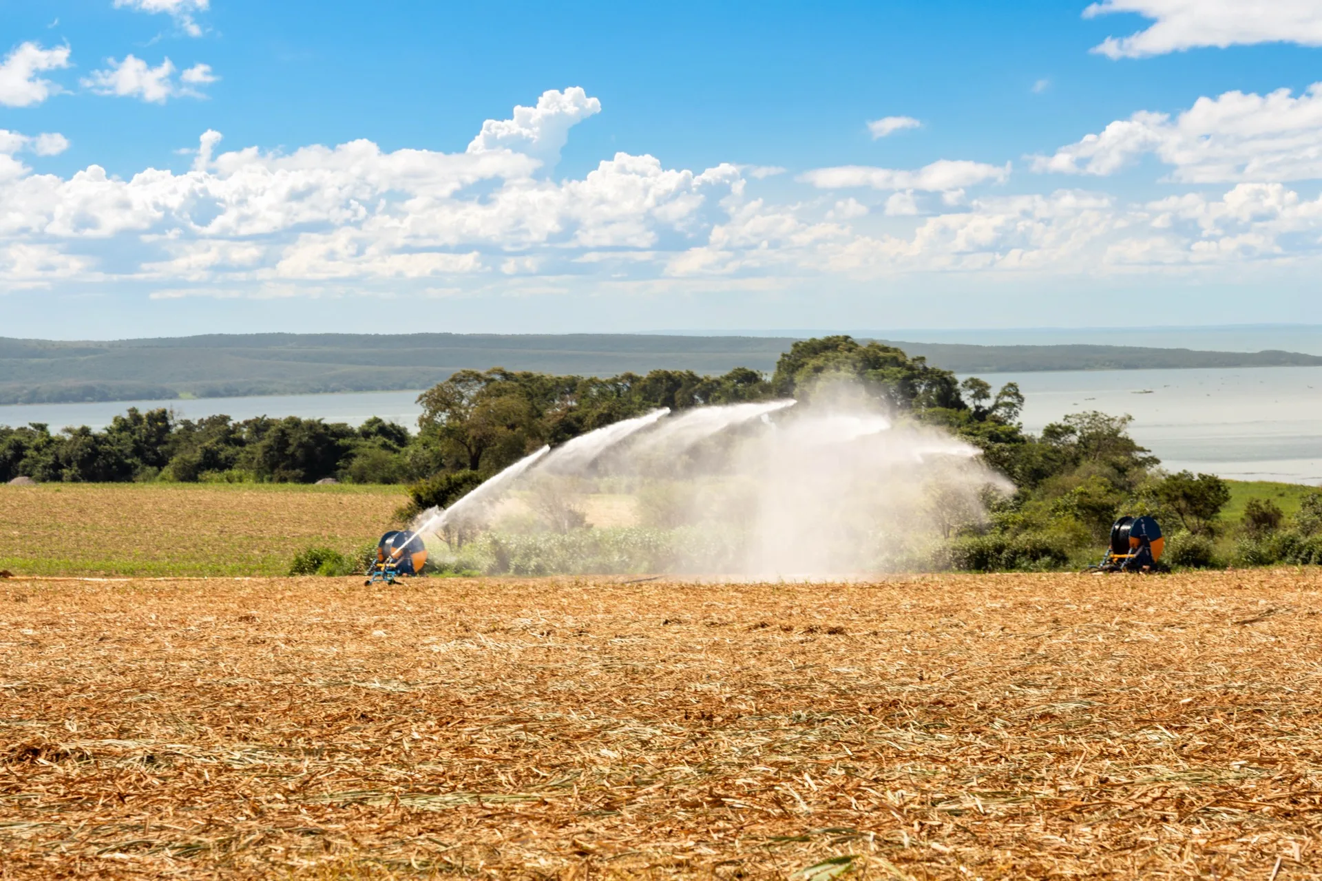 Canhões de fertirrigação aplicando vinhaça sobre a palhada em área agrícola da Da Mata, com a represa ao fundo